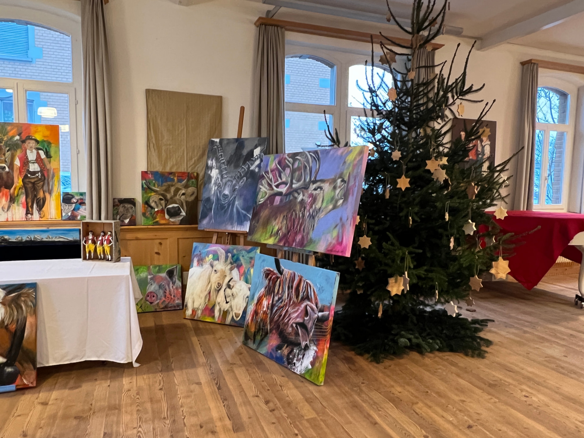 Ausstellung farbenfroher Gemälde mit Tiermotiven neben dem Christbaum